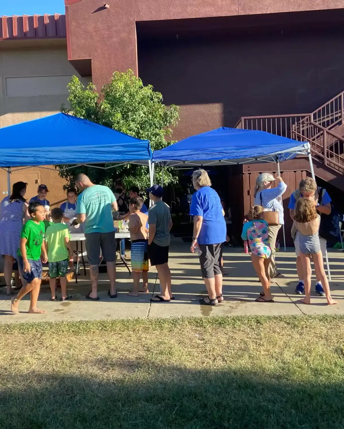 Families gathered under blue pop-up canopies at an outdoor church community event on a sunny afternoon