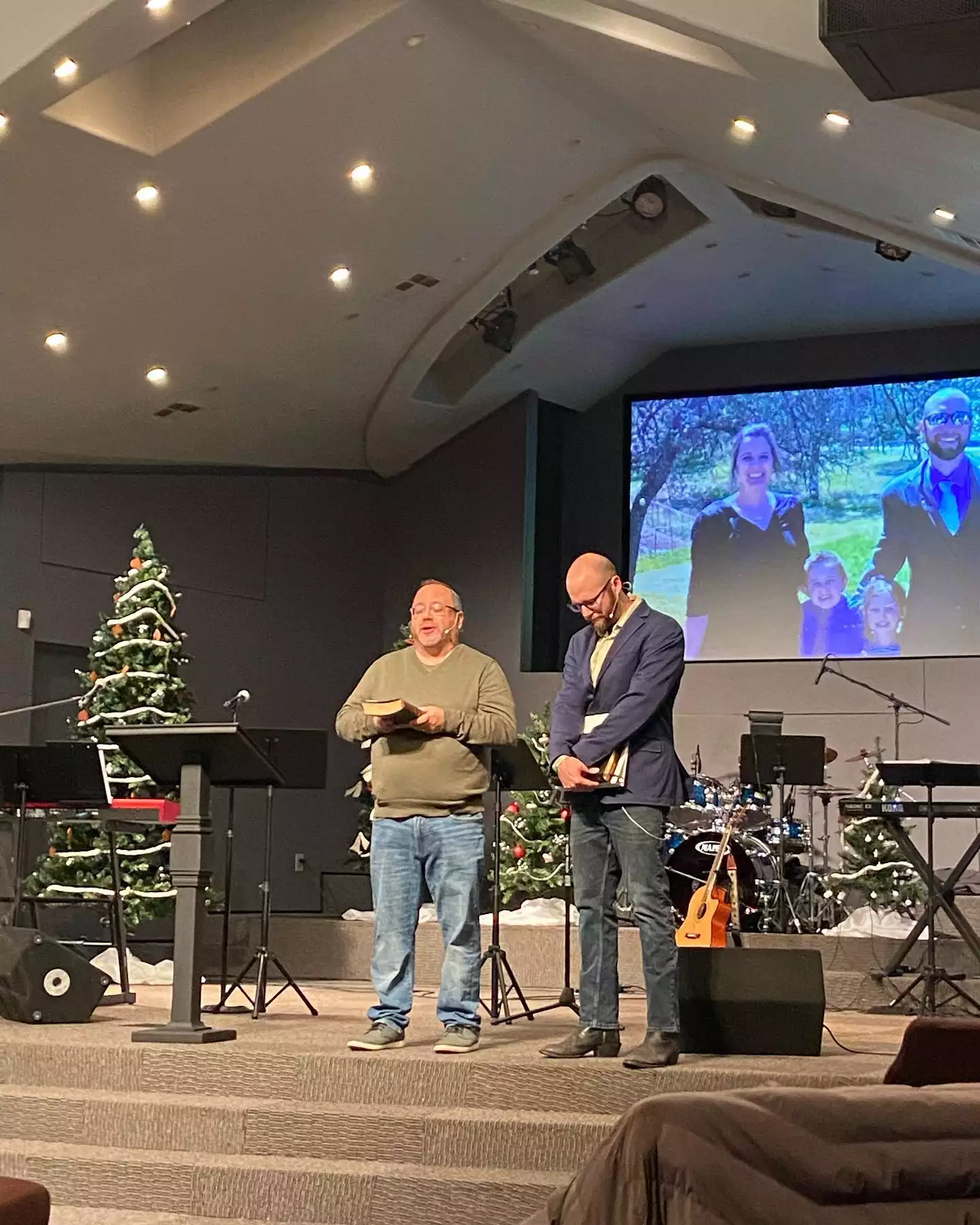 Two men standing together on a church platform during a service, one holding an open Bible