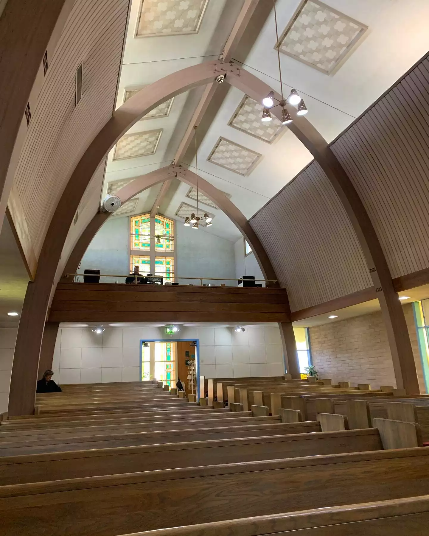 The interior of a church sanctuary with wooden arched beams, a balcony and rows of pews
